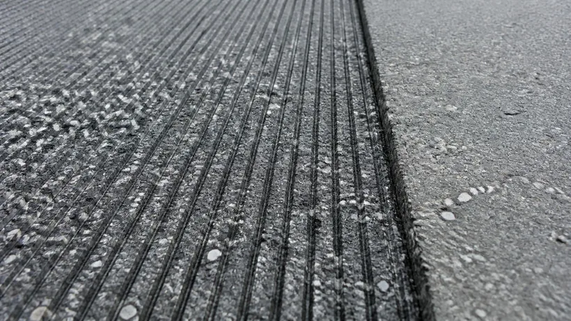 Cold-milled asphalt showing fine parallel grooves and exposed aggregate beside an untouched surface