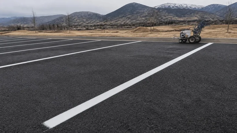 Crisp white stall lines freshly painted on dark asphalt with a striping machine parked at the end of the row
