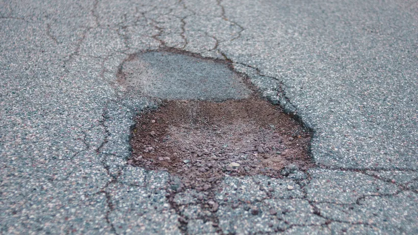 Pothole in asphalt exposing loose aggregate below the surface, with cracks radiating outward into sound pavement
